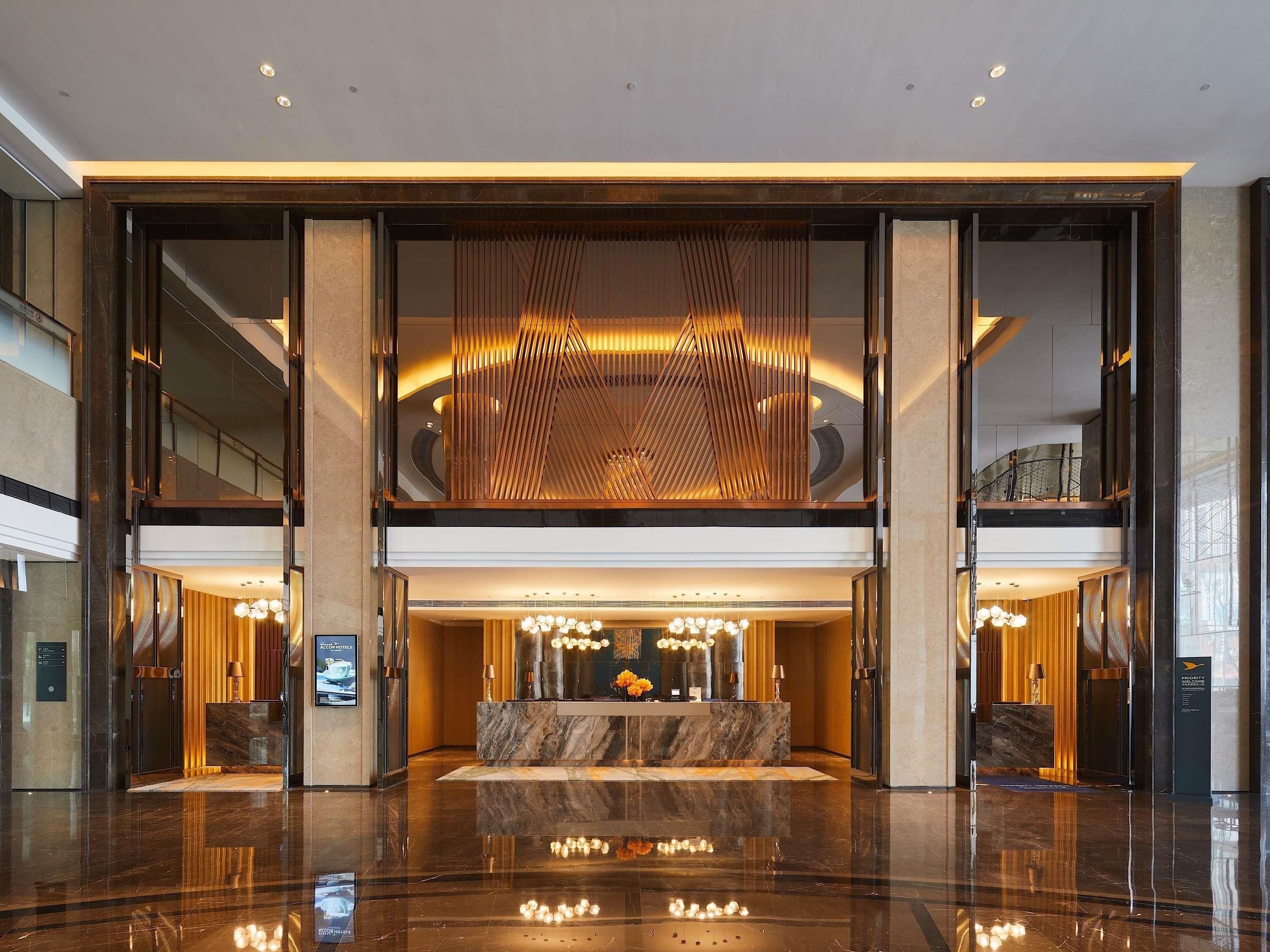 A spacious lobby with a marble reception desk, a seating area, and a modern ceiling design.