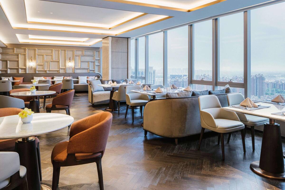 A modern dining area with high ceilings, large windows, and a city view.