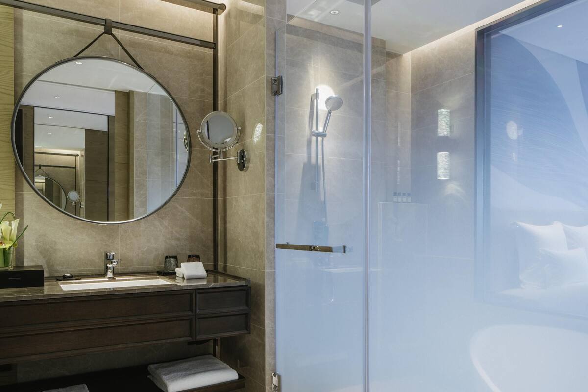 A modern bathroom with a round mirror, a glass-enclosed shower, and a dark wood vanity.