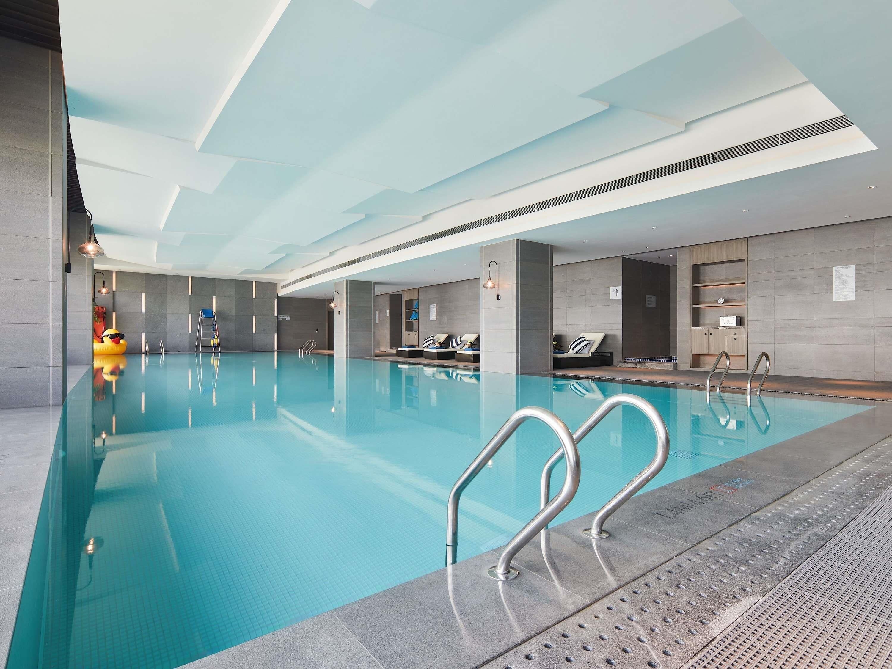 An indoor swimming pool with clear water, metal pool ladders, and a tiled floor.