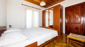 A bedroom with a wooden bed, a wooden bench, a wardrobe, and a mirror. - Apartments Tapera (Dubrovnik)
