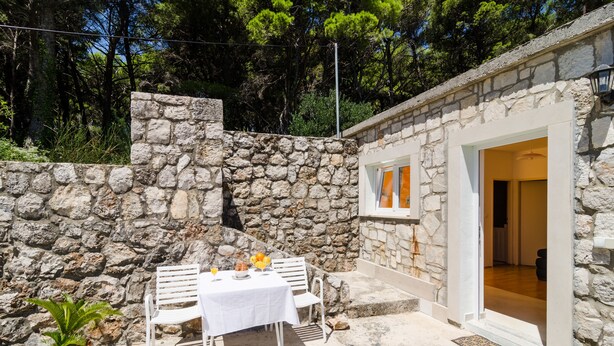 A stone-walled outdoor area with a table and chairs, a potted plant, and a doorway leading to an interior room. - Apartments Tapera (Dubrovnik)