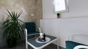 A small, modern room with a tiled wall, a window, a potted plant, a table with a tray, and two chairs. - Apartments Tapera (Dubrovnik)