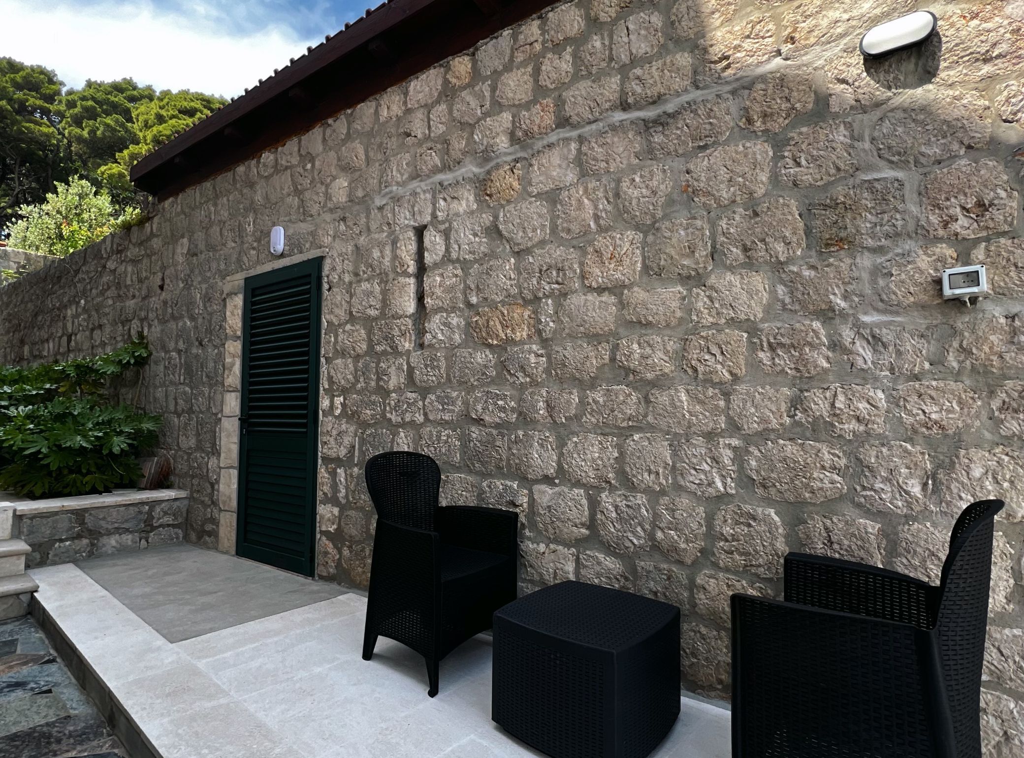 Un edificio in pietra con una porta e due poltrone in vimini nero.
