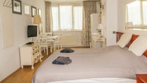 Habitación de hotel con una cama grande, un escritorio, una silla, un televisor y una ventana con cortinas.