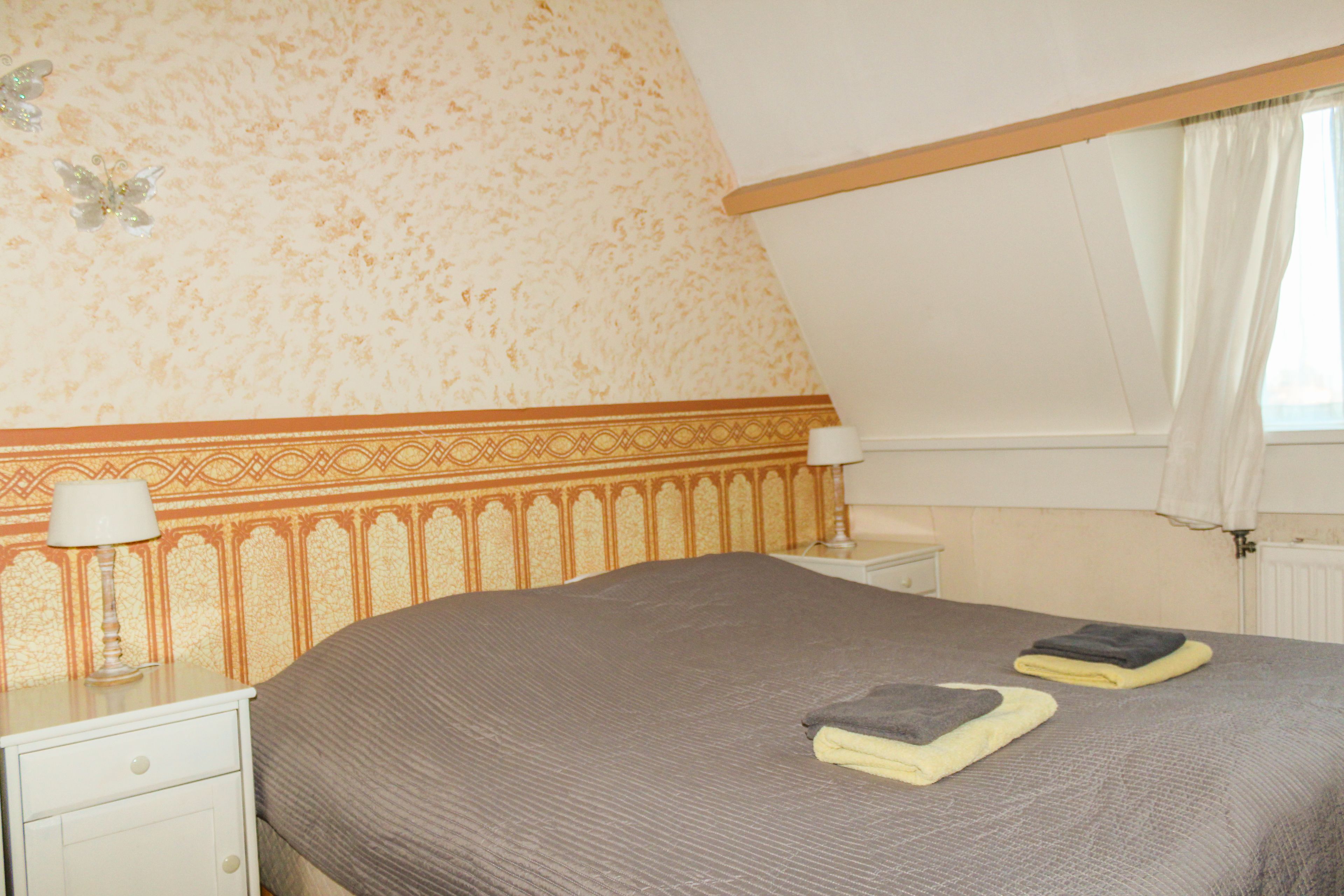 Une chambre avec un grand lit, une table de chevet avec une lampe et un mur décoré d’un motif.