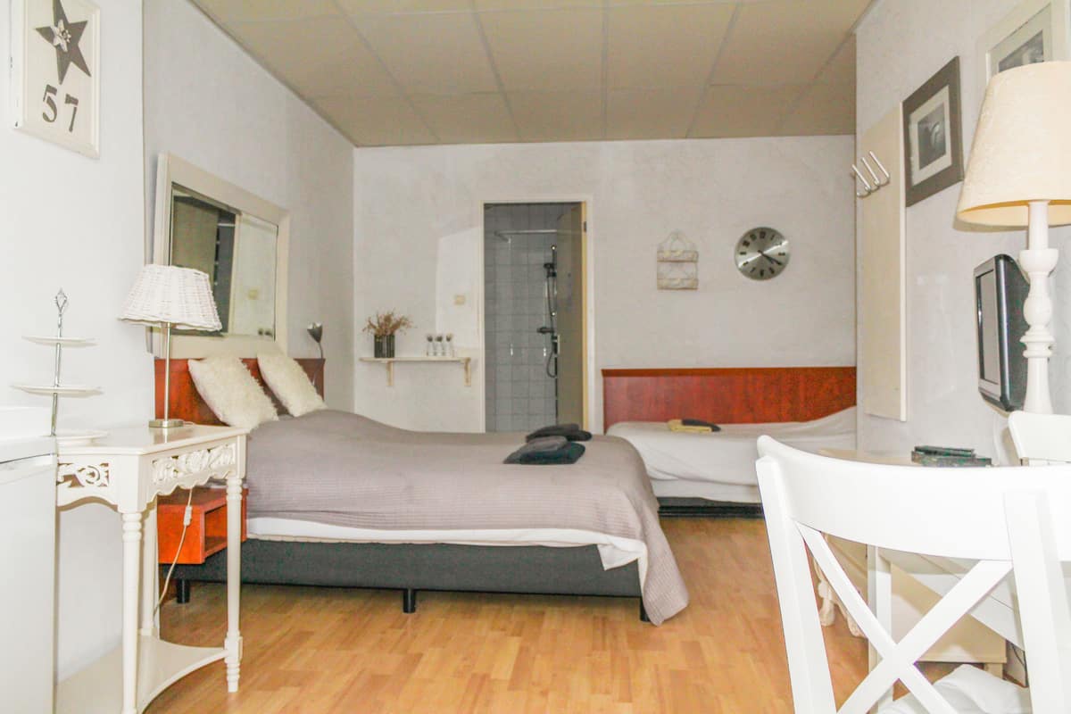 A bedroom with a bed, a chair, a desk, a mirror, a clock, and a door.
