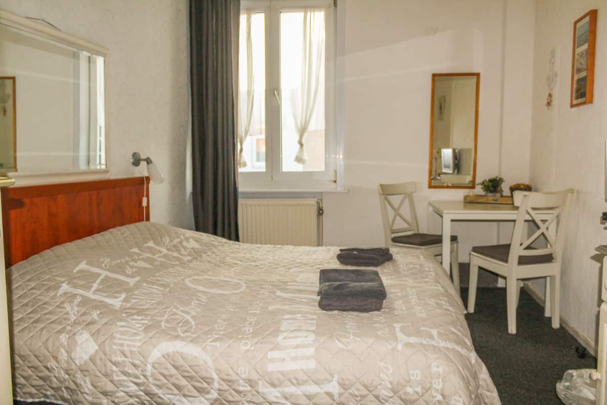 A hotel room with a bed, a desk, a chair, a mirror, and a window with curtains.