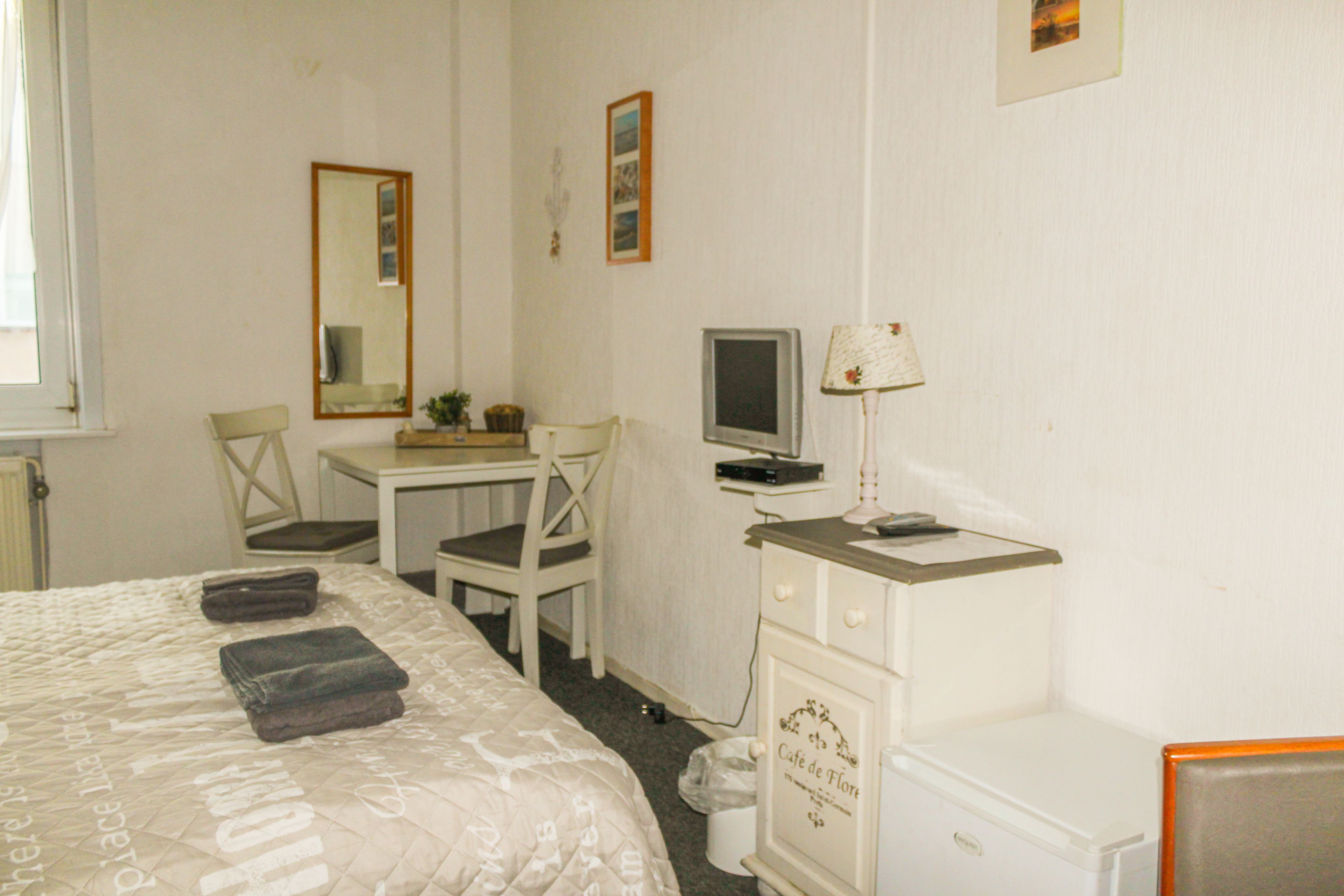 Habitación de hotel con cama, escritorio, computadora, silla, lámpara y un armario pequeño.