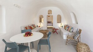 A spacious interior with a white-walled dining area, a sofa with colorful cushions, and a wicker chair. - White Cave Villa by Caldera Houses (Santorini)