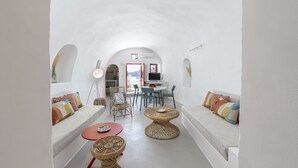 A compact, white-walled room with a sofa, two wicker tables, and a dining area with chairs and a table.