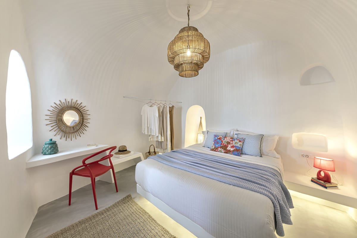 A bedroom with a bed, a desk, a chair, a hanging light fixture, and a mirror on the wall.