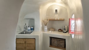 A compact kitchen with a sink, utensils, a vase with dried plants, a bread box, and a coffee maker. - White Cave Villa by Caldera Houses (Santorini)