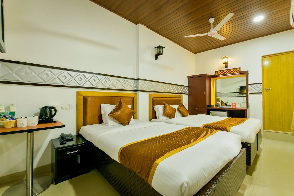A hotel room with two beds, a desk with a telephone, a small cabinet, and a mirror.