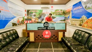 Een hotel receptie met een receptionist, een receptiebalie en twee zwarte leren banken.