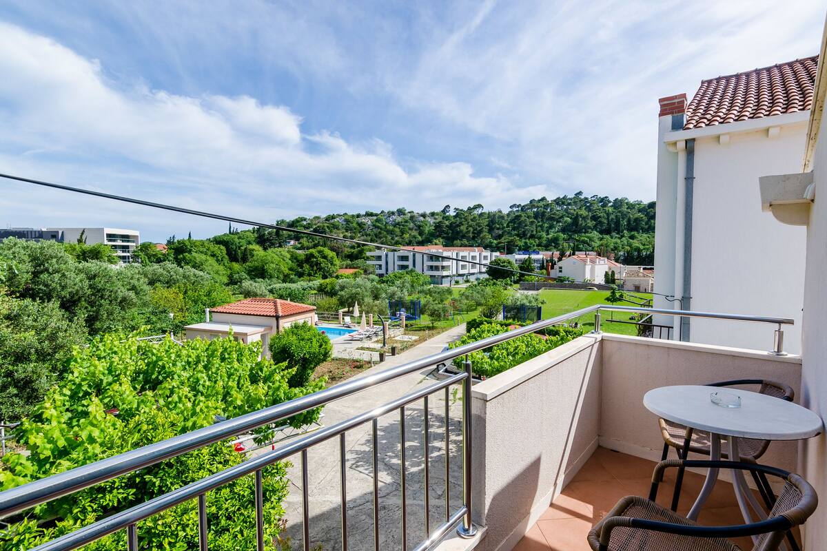 A balcony with a view of a swimming pool, lush greenery, and residential buildings.