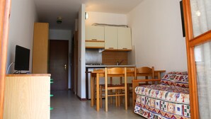 A compact kitchen with a stove, cabinets, and a dining area with chairs and a table. - Condominio Sabbiadoro (Lignano Sabbiadoro)
