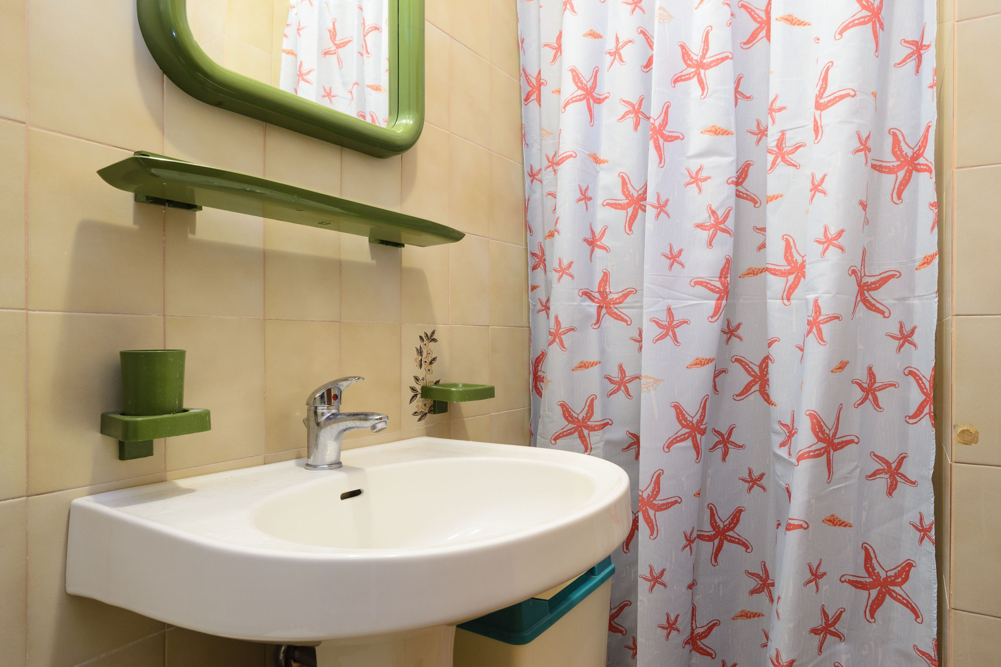 Un baño con lavamanos blanco, toallero verde y cortina de ducha con estampado de estrellas de mar.