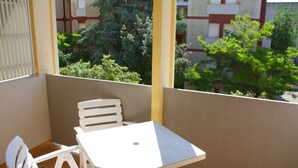 A balcony with a white table and chairs, a yellow pillar, and a view of greenery and buildings. - Condominio Sabbiadoro (Lignano Sabbiadoro)
