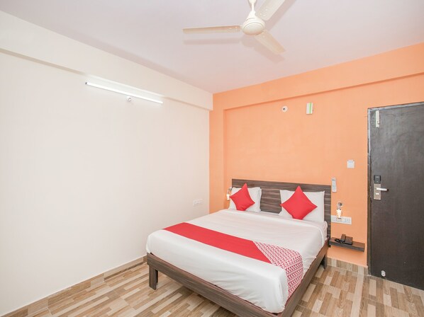 A hotel room with a bed, a ceiling fan, a wall-mounted light, a door, and a bedside table with a phone. - OYO 10480 Hotel PMR (Bengaluru)