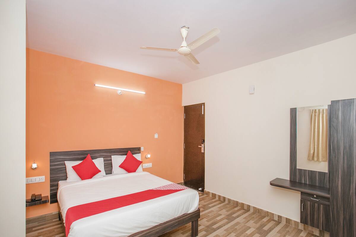 A hotel room with a bed, a ceiling fan, a nightstand, a mirror, and a door.