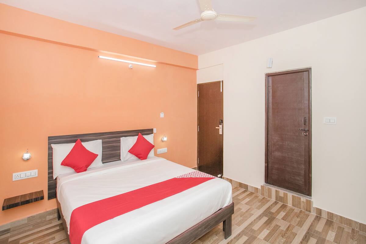 A hotel room with a bed, a ceiling fan, a door, and a light switch.