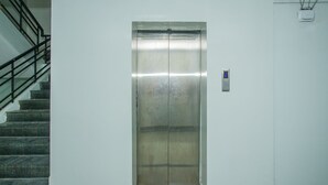 Un ascensor con pantalla digital, una escalera con barandales de metal y una pared lisa.