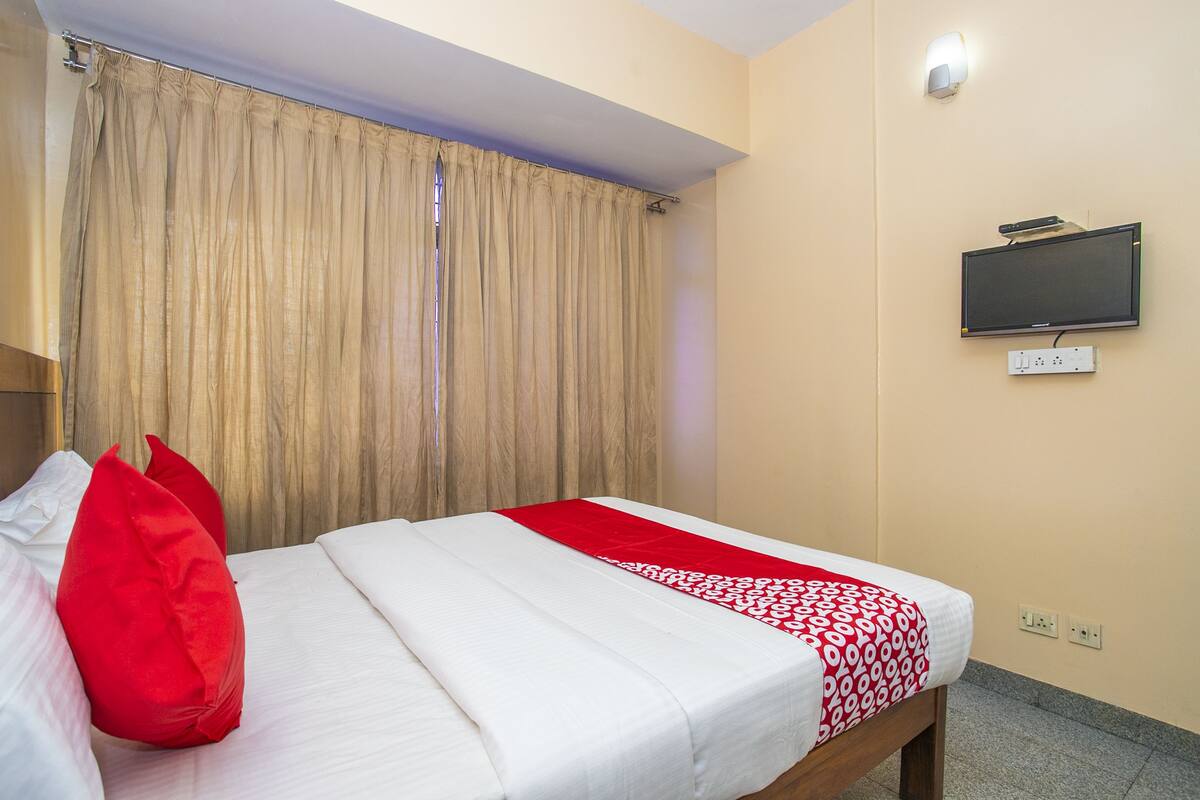 Una habitación de hotel con una cama, un televisor montado en la pared y una ventana con cortinas.