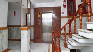 Eine Lobby mit Marmorboden, einer Holztreppe, einem Aufzug und einem an der Wand befestigten Feuerlöscher.