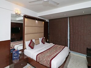 Een hotelkamer met een groot bed, een flatscreen televisie, een plafondventilator en een minibar.