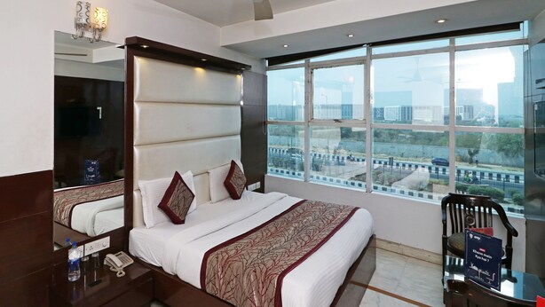 Ein Hotelzimmer mit einem großen Bett, einem Deckenventilator, einem großen Fenster mit Stadtblick, einem Schreibtisch mit Stuhl und einem Spiegel.