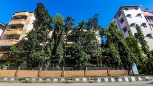 Un edificio de varios pisos con balcones, rodeado de árboles y un cielo azul despejado.