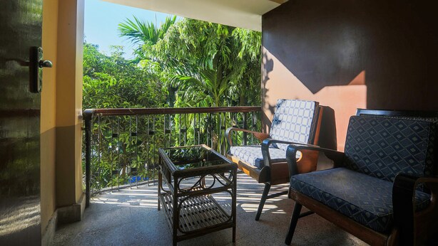 Un balcón con vistas a exuberante vegetación, una mesa de vidrio y dos sillas estampadas.