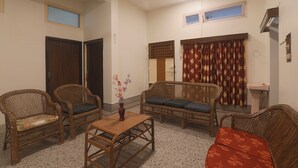 Una sala de estar con muebles de mimbre, una pequeña mesa con un florero y una ventana con cortinas.