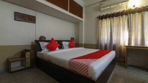 Una habitación de hotel con cama, un escritorio pequeño, un armario y un equipo de aire acondicionado.