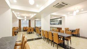 A spacious dining area with multiple tables and chairs, a large window with curtains, and a modern ceiling design.