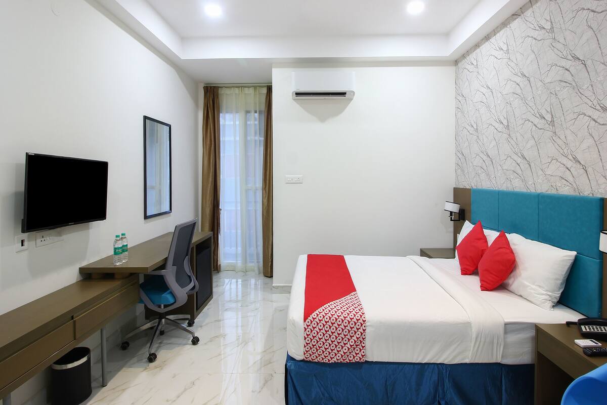 Una habitación de hotel con cama, escritorio, silla, televisor y aire acondicionado.
