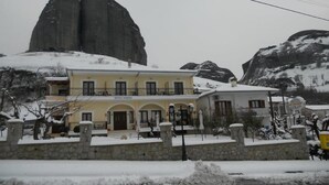 A hotel with a yellow facade, a balcony, and a stone wall in front. - Gogos Hotel (Kalabaka)