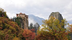 A historic stone building perched on a cliff with a mountainous backdrop. - Gogos Hotel (Kalabaka)