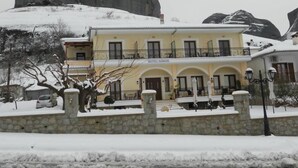 A two-story hotel with a balcony and a stone wall in front. - Gogos Hotel (Kalabaka)