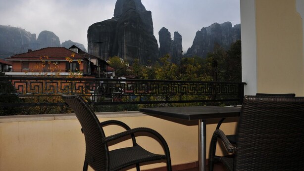 A balcony with wicker chairs and a table, overlooking a mountainous landscape with a building in the background. - Gogos Hotel (Kalabaka)