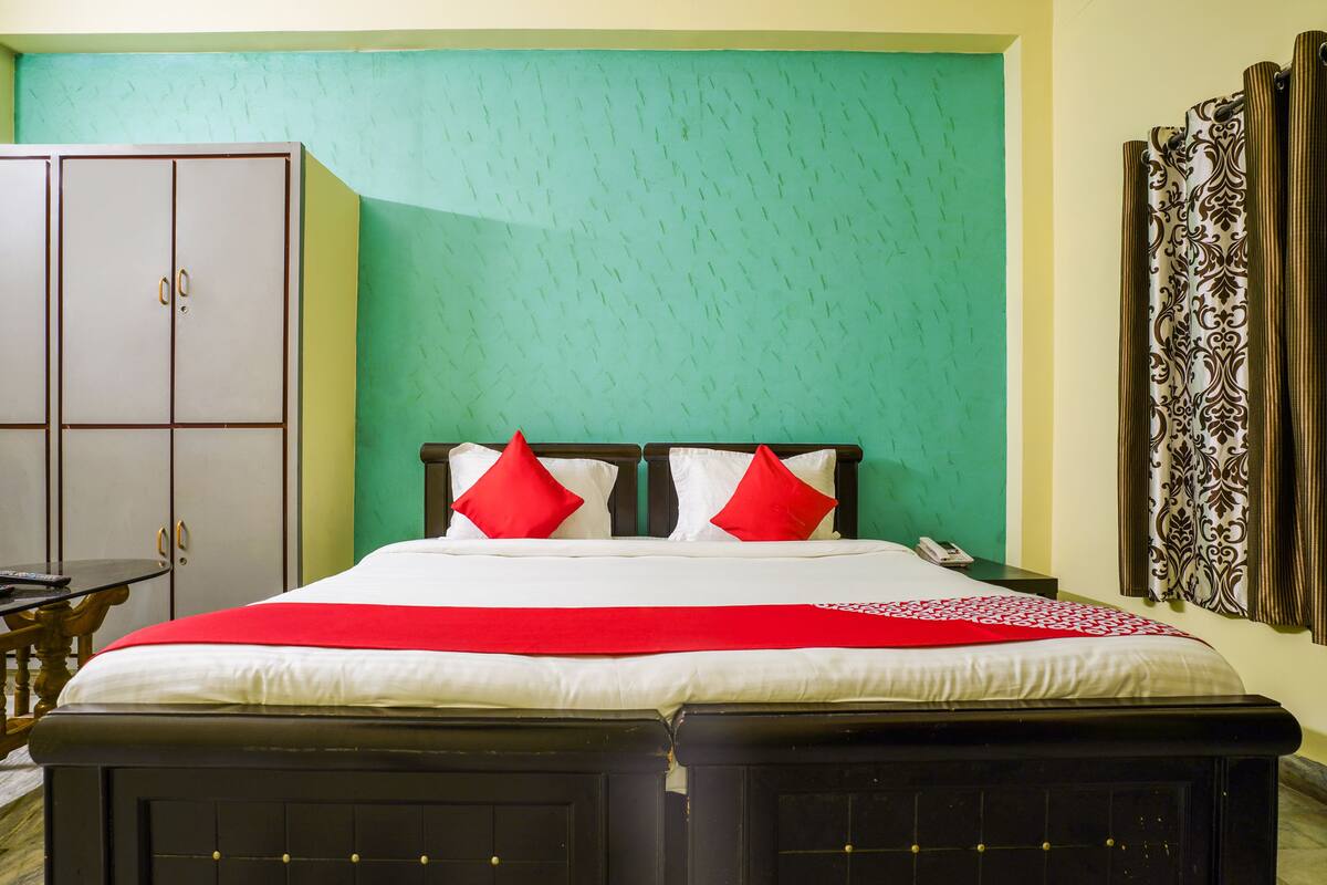 A double bed with two red pillows, a bedside table, a wardrobe, and a patterned curtain.