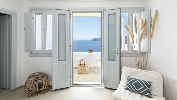 A room with a view of the sea, a wicker chair, a white sofa with a patterned pillow, and a small table with a basket. - Big Blue Villa by Caldera Houses (Santorini)