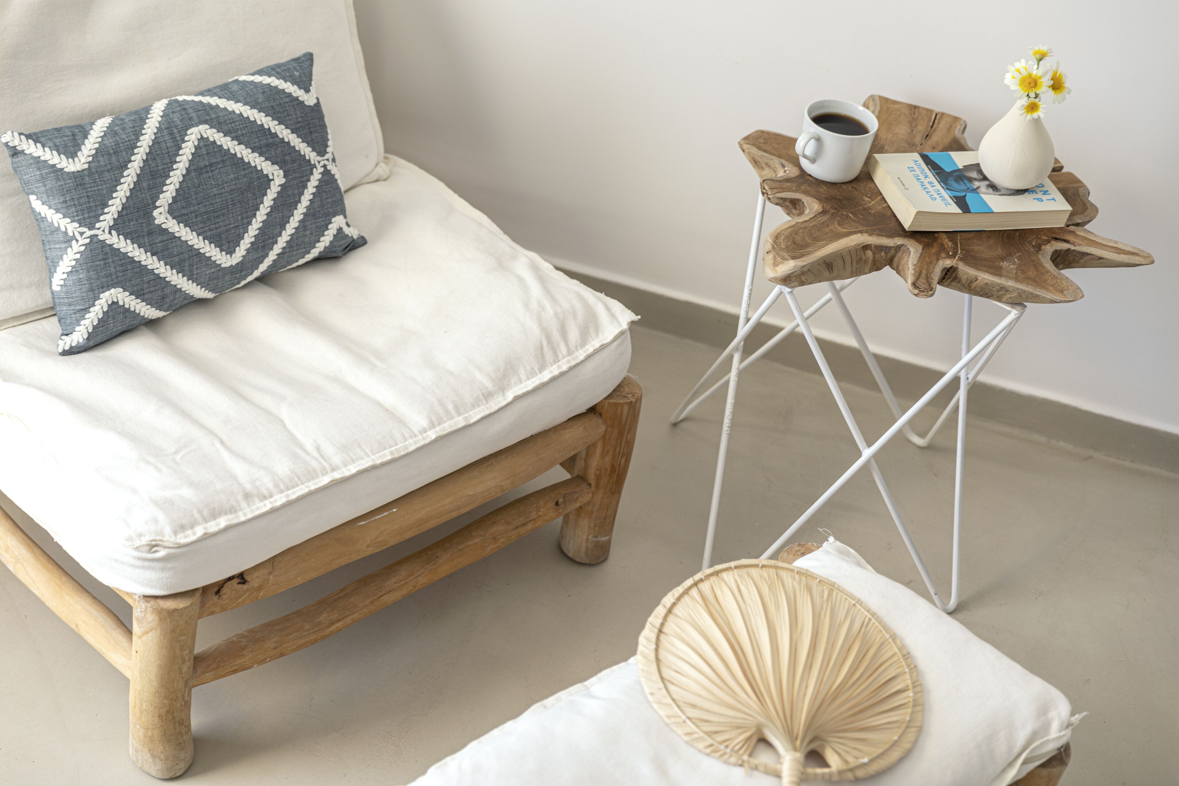 Um quarto aconchegante com uma cama de madeira, uma pequena mesa de cabeceira de madeira com um livro, uma xícara e um vaso com flores.