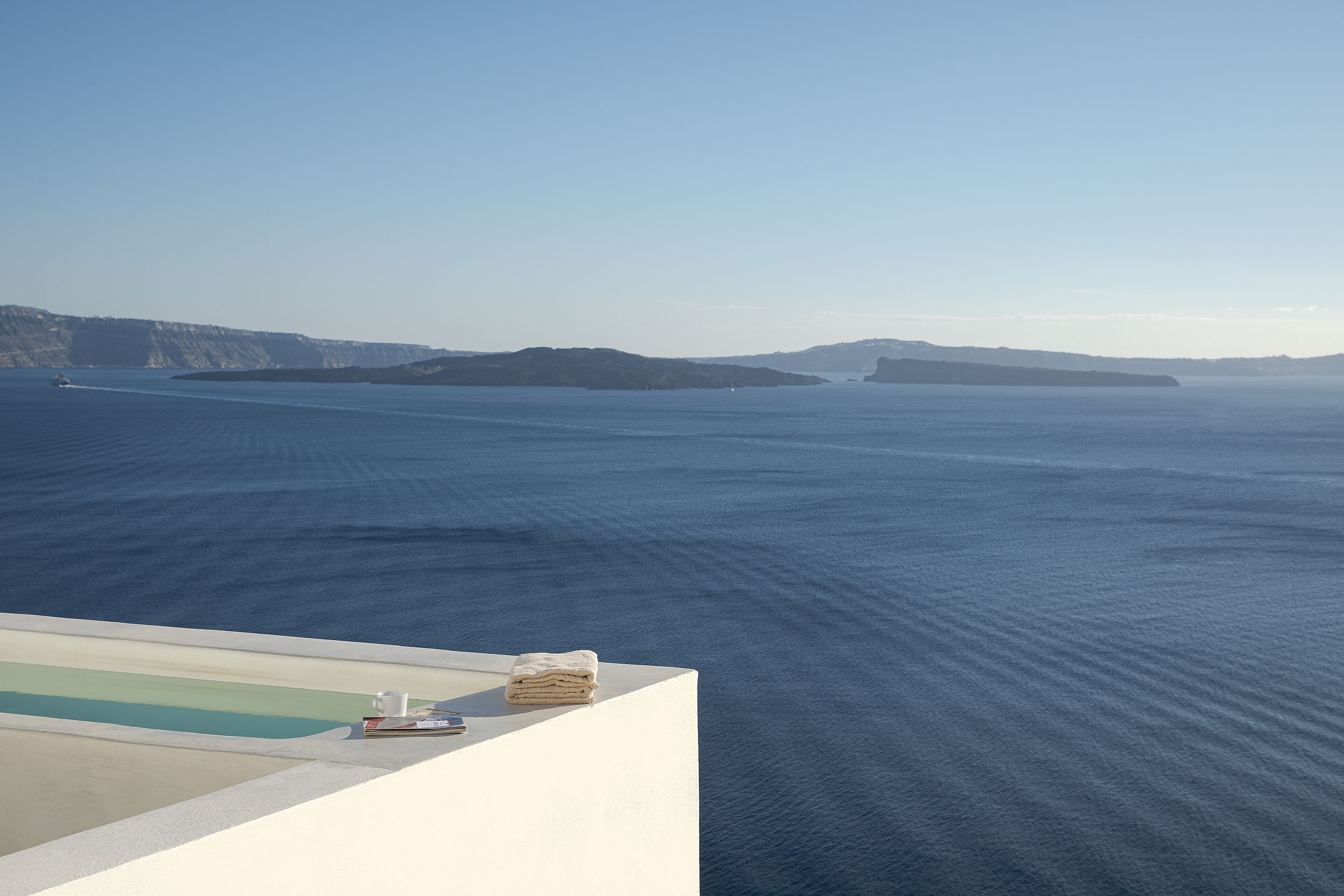 A view of a large body of water with distant landforms, a white structure with a pool, and a stack of towels.