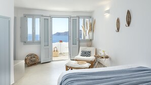 A bedroom with a bed, a chair, a small table, and a view of the sea through open doors. - Big Blue Villa by Caldera Houses (Santorini)