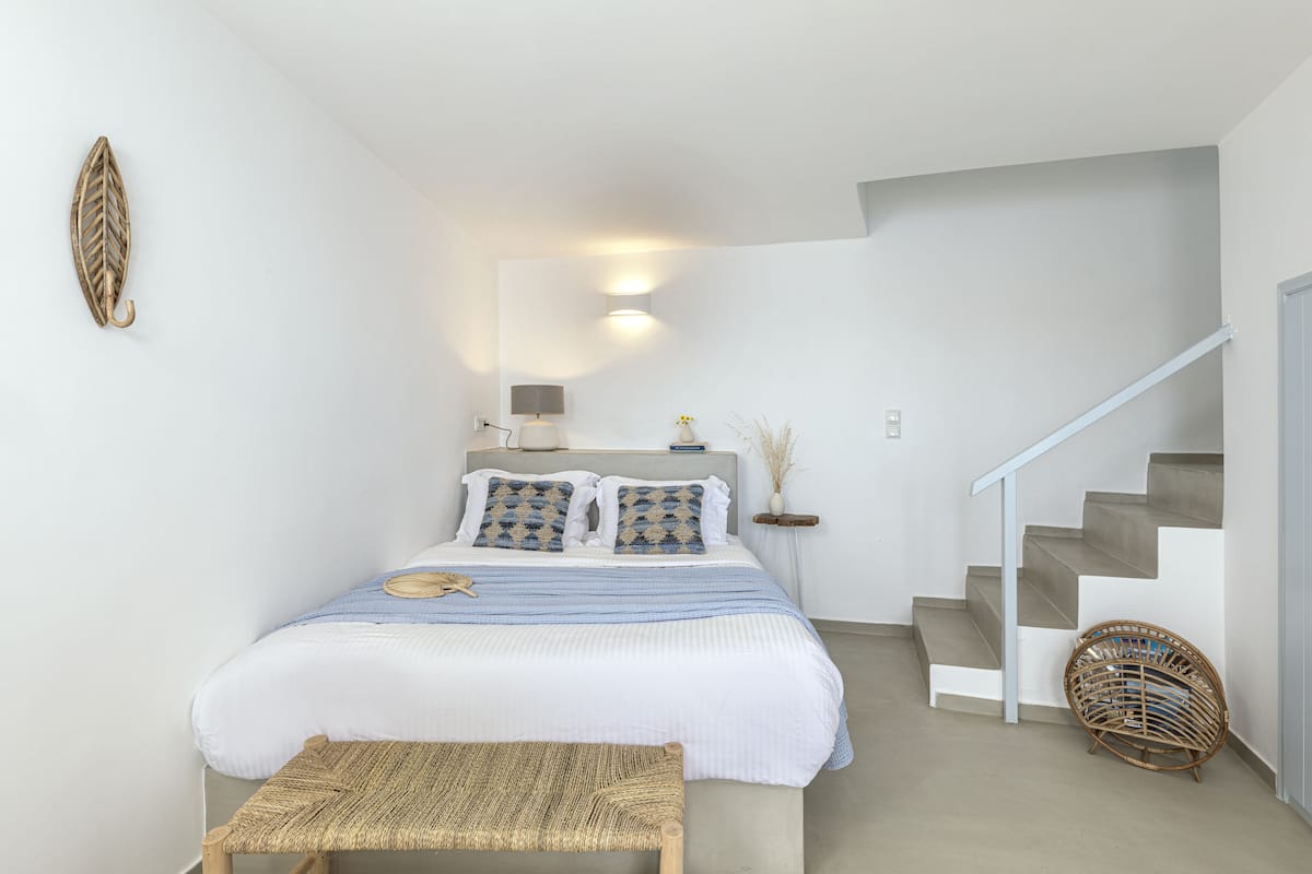 Un dormitorio con cama, un banco, una lámpara de pared, una mesita de noche y una escalera.