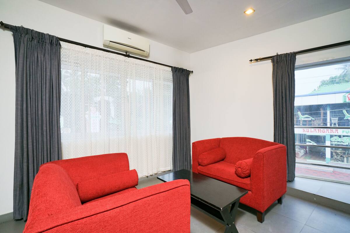 A room with two red sofas, a black coffee table, and a large window with grey curtains.