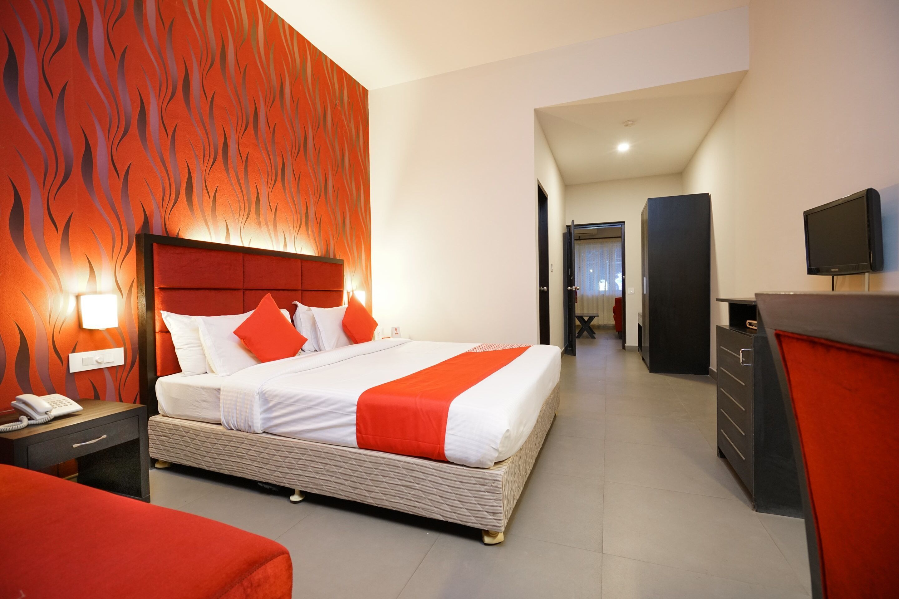 A modern hotel room with a large bed, a desk, a TV, and a wardrobe.
