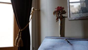 A room with a window, a curtain, a vase with dried flowers, and a framed picture on the wall.